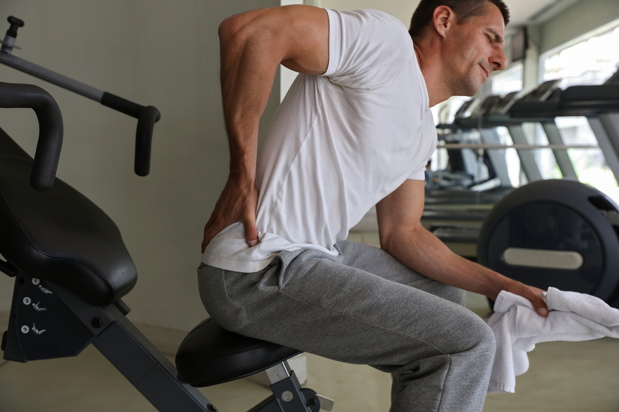Man with low back pain in gym. Sports exercising injury. Man needs chiropractic services
